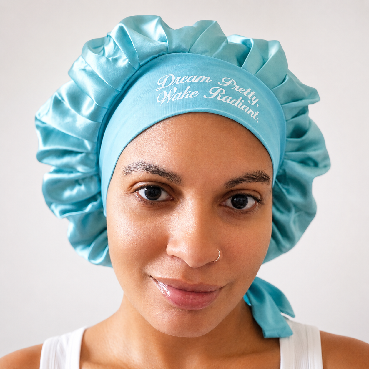 Woman wearing a satin bonnet with the words "Dream Pretty, Wake Radiant" printed on it