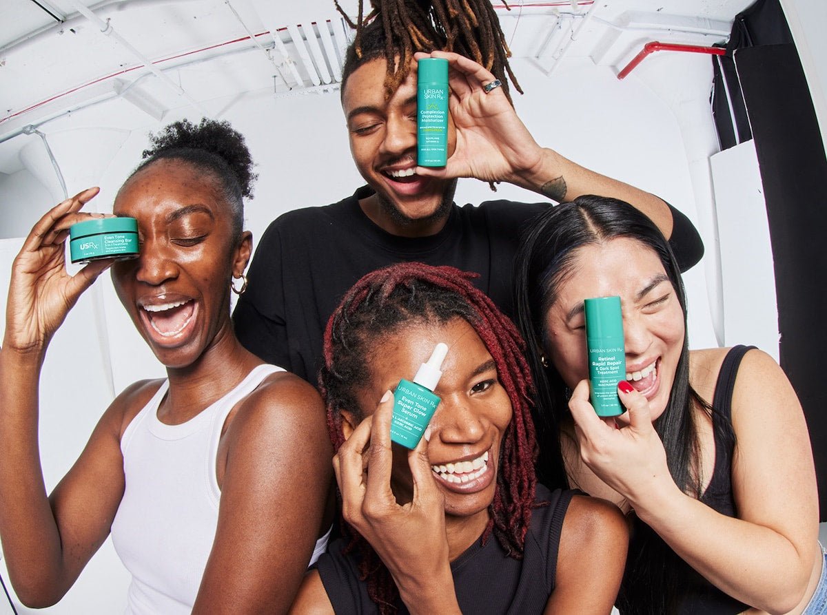 Four people smiling and holding different USRx skincare products against a white background
